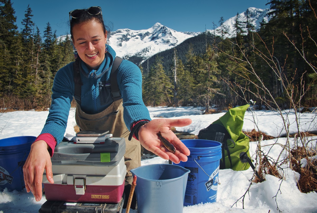 Lindsey holding a juvenile salmon with mountain background