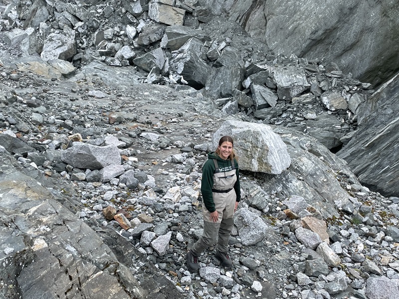 woman standing among rocks next to a stream