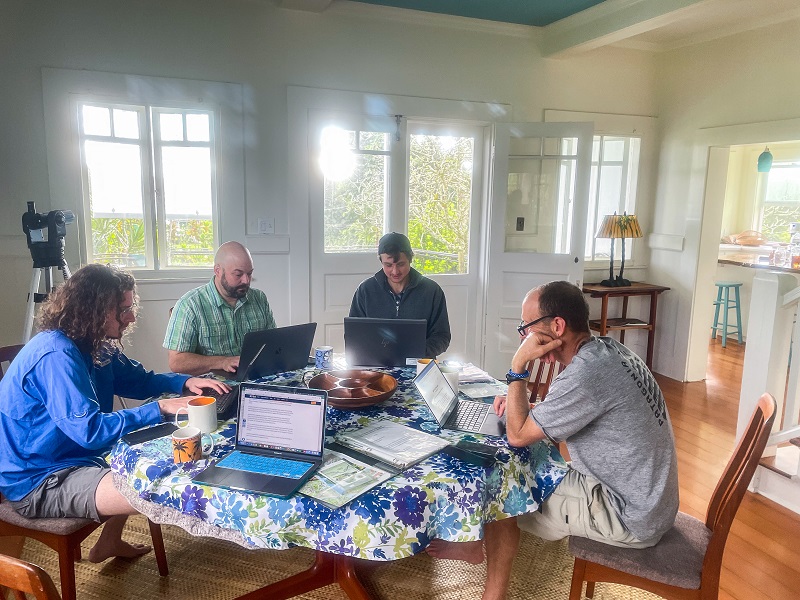 a group of people sit around a table on laptops