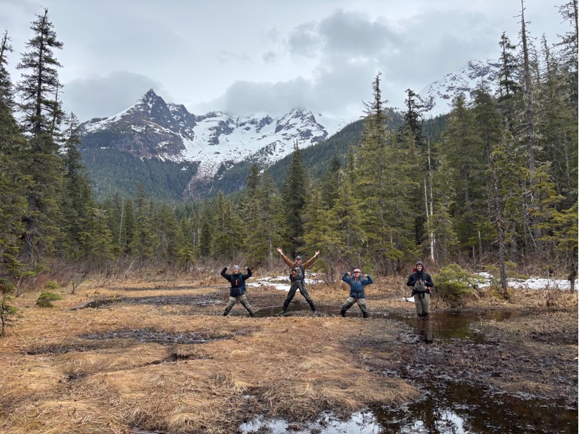 four ACRC interns pose in a meadow with snow-capped mountains in the background