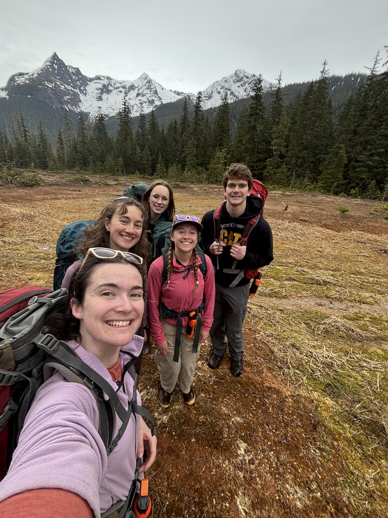 a group of ACRC interns pose for a photo in a field with mountains in the background